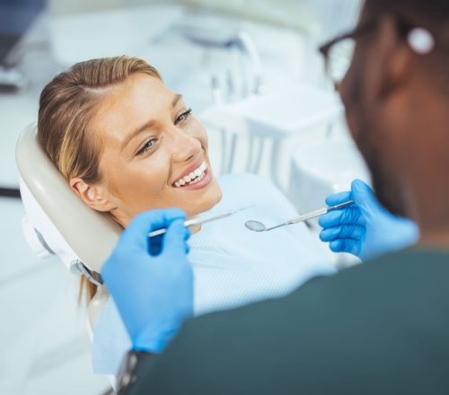 Closeup shot professional dentist with protective surgical mask, doing check up of patient. Dentist examining smiling female patient in clinic. Male is checking smiling patient in examination room.